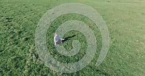 Low orbital flight around man on green grass with notebook pad at yellow rural field.