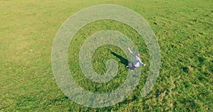 Low orbital flight around man on green grass with notebook pad at yellow rural field.