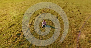 Low orbital flight around man on green grass with notebook pad at yellow rural field.