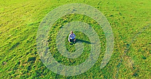 Low orbital flight around man on green grass with notebook pad at yellow rural field.