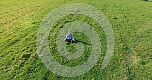 Low orbital flight around man on green grass with notebook pad at yellow rural field.