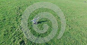 Low orbital flight around man on green grass with notebook pad at yellow rural field.