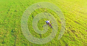 Low orbital flight around man on green grass with notebook pad at yellow rural field.