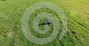 Low orbital flight around man on green grass with notebook pad at yellow rural field.