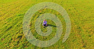 Low orbital flight around man on green grass with notebook pad at yellow rural field.