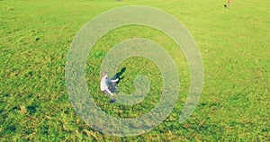 Low orbital flight around man on green grass with notebook pad at yellow rural field.