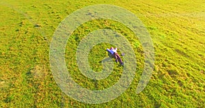 Low orbital flight around man on green grass with notebook pad at yellow rural field.