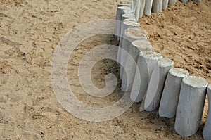 Low palisade of logs in a sandbox bordering a play area on a playground from a path in the sand