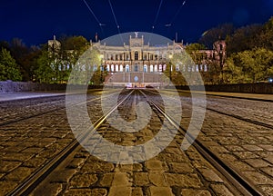 Low perspective symmetrical view over a tram track with popular Munich architecture in the background at night.