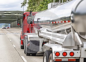 Low profile pro red big rig semi truck transporting cargo in tank semi trailer running on the road with truss bridge