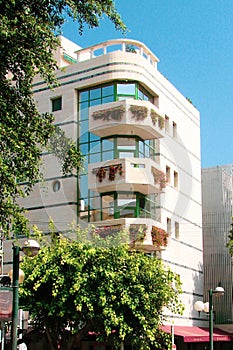 A low-rise building with a bright facade, large glass windows and large balconies with interesting plants that wrap around them.