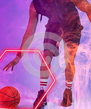 Low section of biracial basketball player dribbling ball by glowing hexagon on violet background