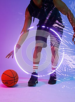 Low section of biracial basketball player dribbling ball by illuminated circle and plants