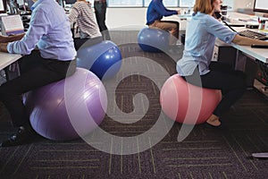 Low section of business people sitting on exercise balls while working at office