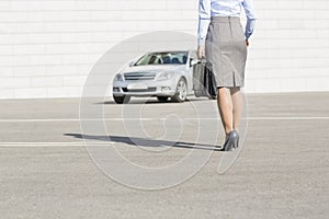 Low section of businesswoman carrying briefcase while walking towards car on street