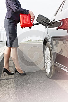 Low section of businesswoman fueling car on road with canister