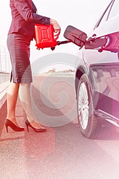 Low section of businesswoman fueling car on road with canister