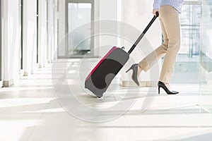 Low section of businesswoman with luggage exiting airport photo