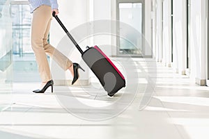 Low section of businesswoman with luggage exiting airport photo