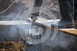 Low section of construction worker using jackhammer drill to breaking reinforced concrete pillar in construction site