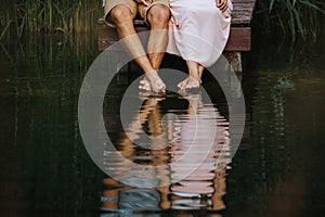 Low section of a couple with their feet in the water of a lake and a reflection