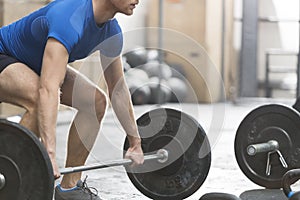 Low section of dedicated man lifting barbell in crossfit gym