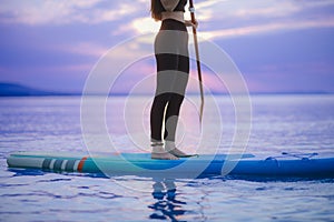 Low section of girl surfer paddling on surfboard on the lake at sunrise, lowsection.