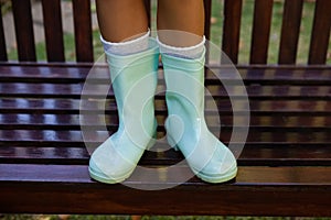 Low section of girl wearing green rubber boot standing on wooden bench