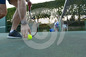 Low section of man holding tennis racket picking up ball on outdoor tennis court, with copy space