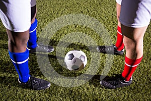 Low section of players standing by soccer ball