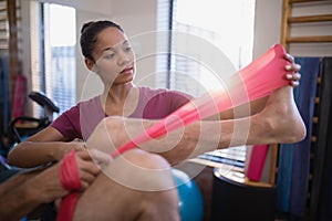 Low section of senior male patient pulling resistance band by female therapist