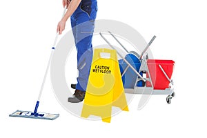 Low section of servant mopping floor by wet floor sign photo