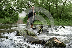 Low section shot of stream with hiker with a backpack crossing a river