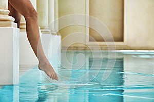 Low section of woman by poolside feeling the water temperature