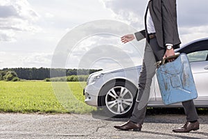 Low section of young businessman with gas can walking by broken down car at countryside