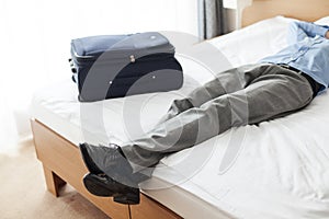 Low section of young businessman sleeping beside suitcase in hotel room