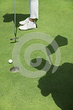 Low section of young woman hitting the ball on the golf course, focus on the hole