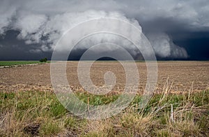 A low shelf cloud under a thunderstorm almost touches the ground over a field.