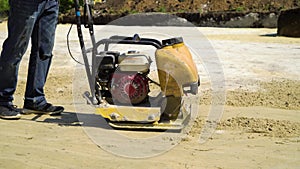 Low shot of man ramming sand surface with vibratory plate compactor