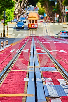 Low streetcar tracks view of road with oncoming blurry trolley coming uphill with vehicle, San Francisco, CA