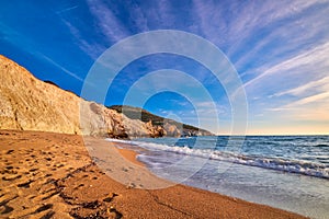 Low sun over beach, cliffs and hills and deep azure sea. Agios Ioannis beach, Milos island, Greece.