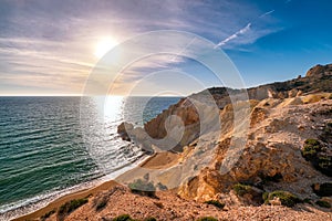 Low sun over beach, cliffs and hills and deep azure sea. Agios Ioannis beach, Milos island, Greece.