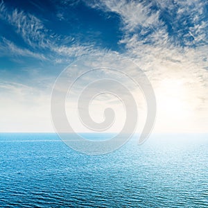 Low sun in white clouds over blue sea