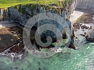 Low tide period and aerial view on ocean bed and chalk cliffs of Porte d`Aval arch in Etretat, Normandy, France. Tourists