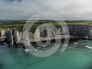 Low tide period and aerial view on ocean bed and chalk cliffs of Porte d`Aval arch in Etretat, Normandy, France. Tourists