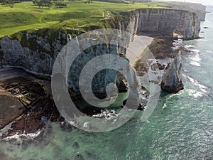 Low tide period and aerial view on ocean bed and chalk cliffs of Porte d`Aval arch in Etretat, Normandy, France. Tourists photo