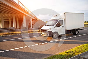 A low-tonnage commercial refrigerated van transports perishable products in the summer on a country road against the