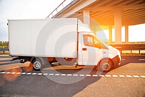 A low-tonnage commercial refrigerated van transports perishable products in the summer on a country road against the photo