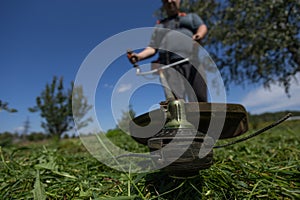 Low viewing angle. On a clear day, a man mows the grass in his backyard with a lawn mower. A man holding a lawnmower