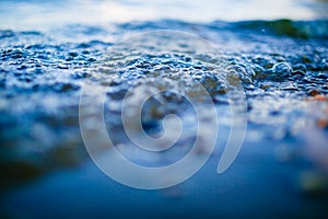 Low wave bubbles reaching coastline macro. Water texture